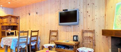 A wooden interior with a television mounted on the wall, a fireplace, and a dining area with wooden furniture.