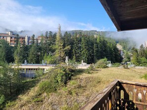 A mountainous landscape with buildings, trees, and a wooden deck. - Bright studio with mountain view - 4 guests (Pra-Loup)