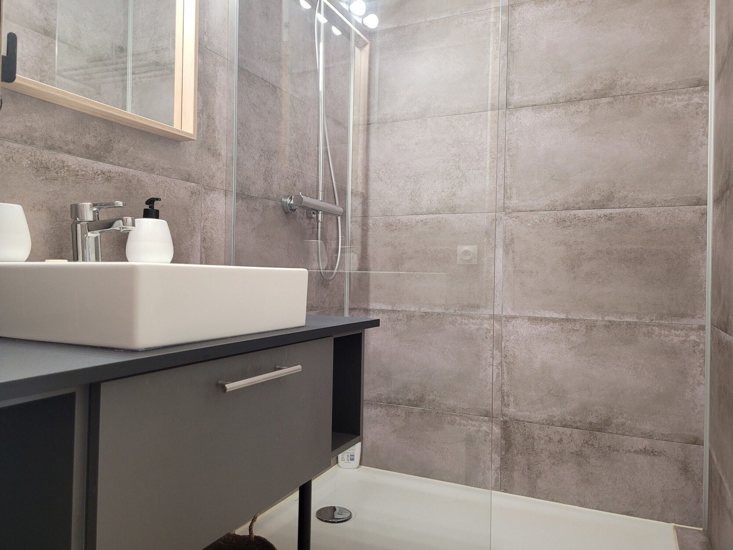A modern bathroom with a white sink, a mirror, and a shower enclosure.