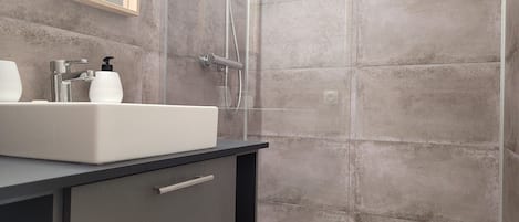A modern bathroom with a white sink, a mirror, and a shower enclosure.