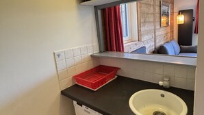 A compact bathroom with a white sink, a red basket, and a window with red curtains. - Comfortable apartment with south-facing balcony - 4 guests (Avoriaz)