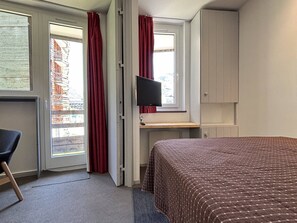 Ein Hotelzimmer mit einem Bett, einem Schreibtisch mit Computer, einem Sessel und einem Fernseher.