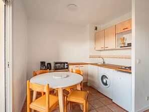 Cuina compacta amb taula rodona, cadires de fusta, rentadora, microones i cafetera.