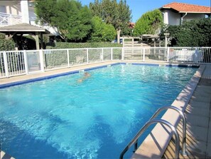 A swimming pool with a metal ladder, surrounded by a white fence, and trees in the background. - Apartment with shared pool, parking - 4 guests (Biarritz)