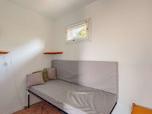 Habitació petita amb un llit individual, una finestra, una estant de fusta i un terra de rajola.