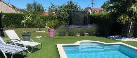 Un patio trasero con piscina, césped artificial y algunas sillas de descanso.