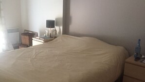 Quarto com cama, mesa de cabeceira, abajur e prateleira na parede.