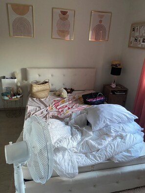 Ein Schlafzimmer mit einem Bett, einem Nachttisch mit Lampe, einer Wanduhr und gerahmten Kunstwerken.