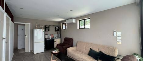 A modern living space with a sofa, a coffee table, a dining area with a refrigerator, and a small window.