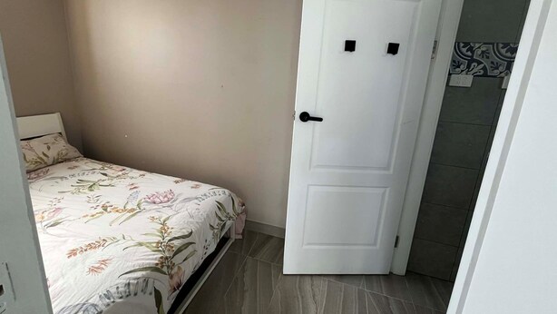 Makuuhuone, jossa on sänky, ovi ja laatoitettu lattia.