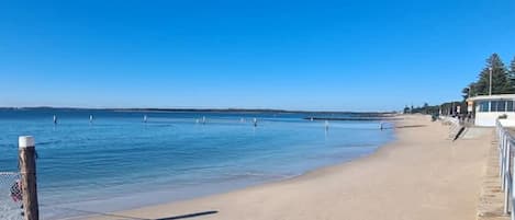 A beach with a clear sky, a sandy shore, and a building with a white facade.