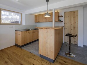 A modern kitchen with wooden cabinets, a central island, and a bar stool. - Guarda Val Müller Erlenstube Wohnung Erlenstube Wohnung Erlenstube by Interhome (Lantsch)