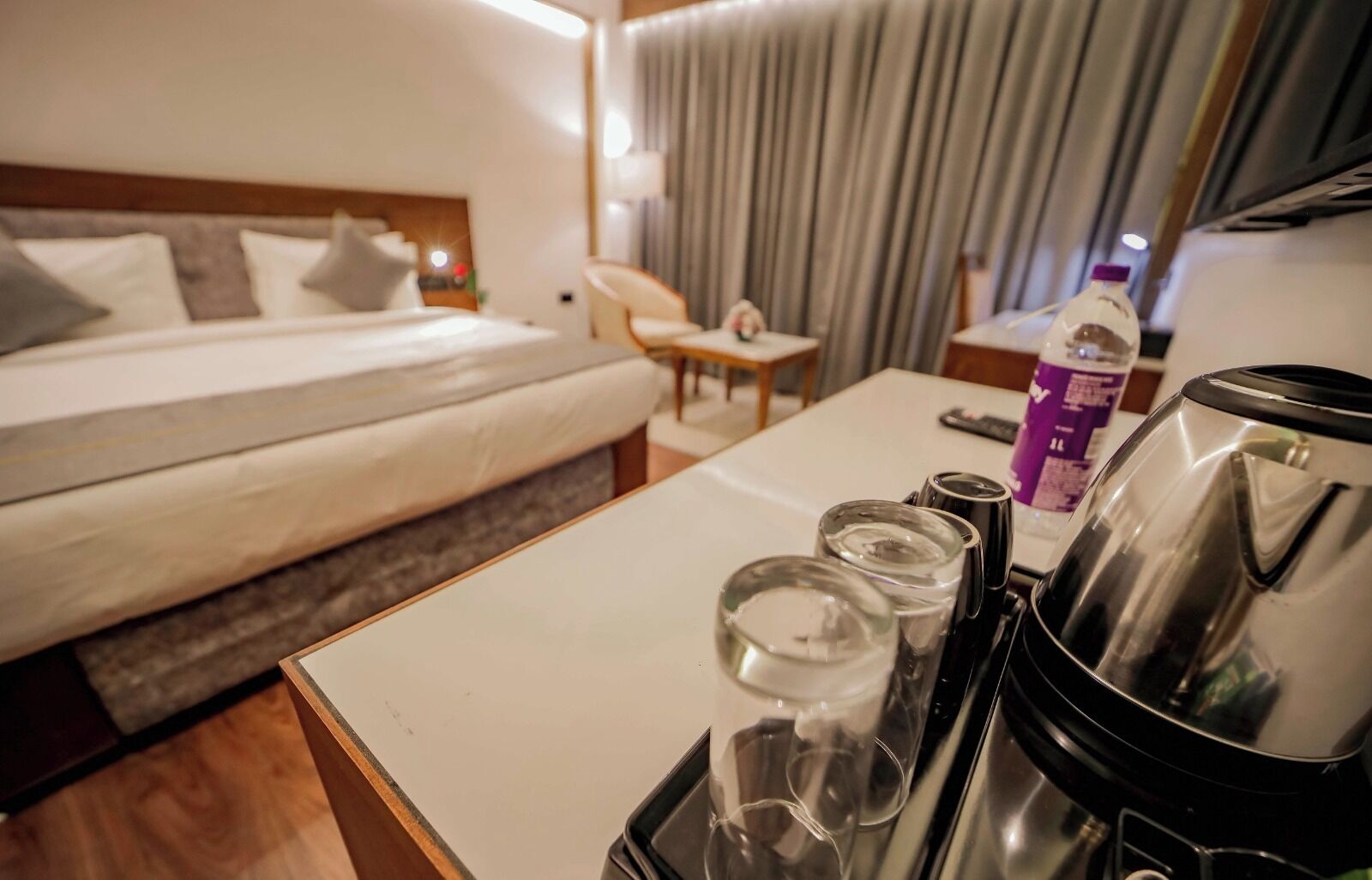 Een hotelkamer met een bed, een tafel met waterkoker, glazen en een fles.