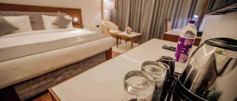 Habitación de hotel con cama, una mesa y una tetera, vasos y una botella.