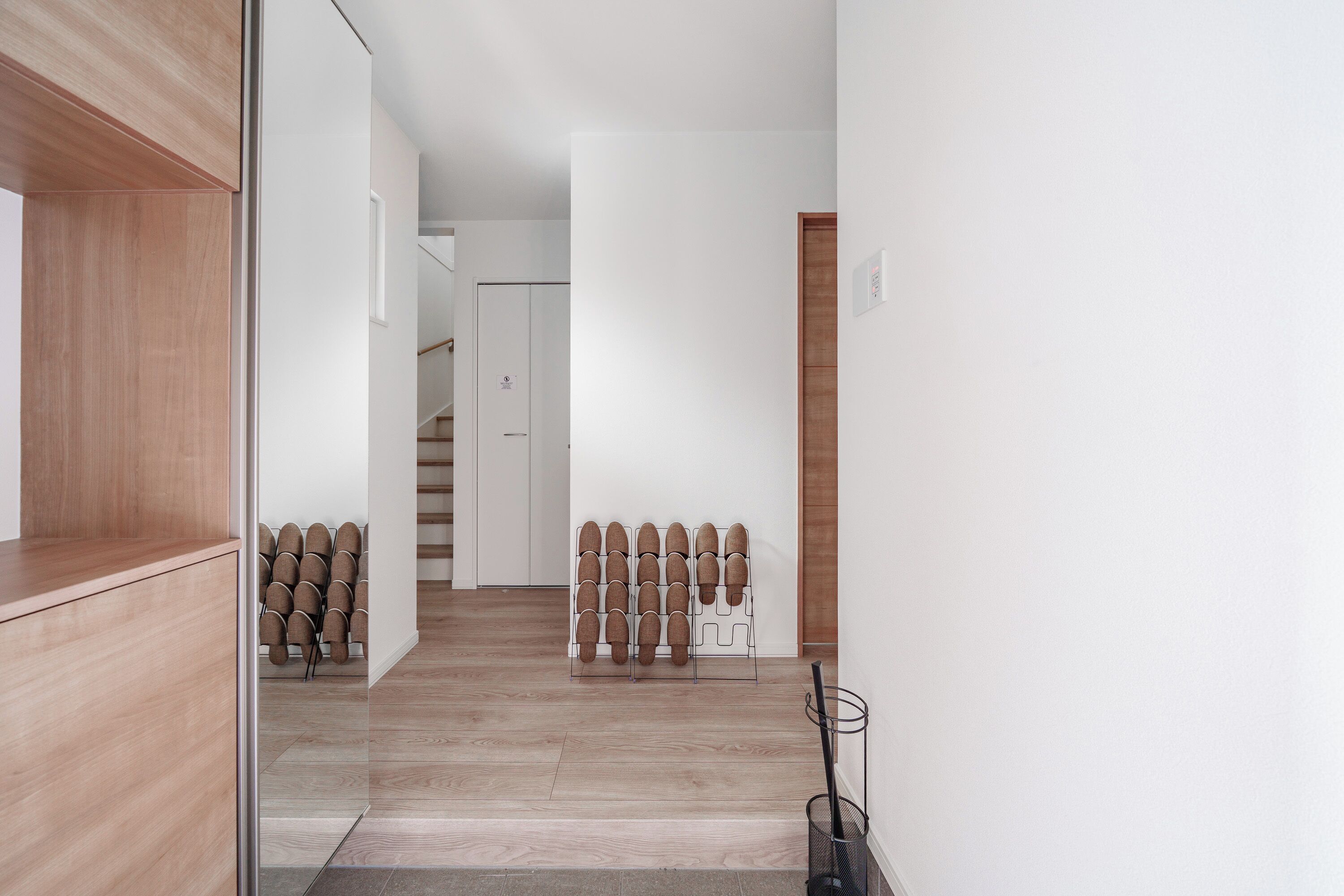 A hallway with wooden flooring, a shoe rack, and a door leading to a staircase.