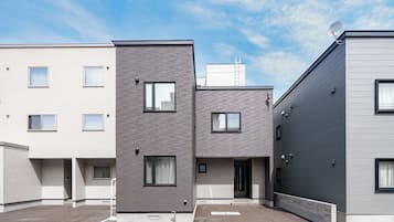 A modern multi-story residential building with a flat roof, multiple windows, and a satellite dish.