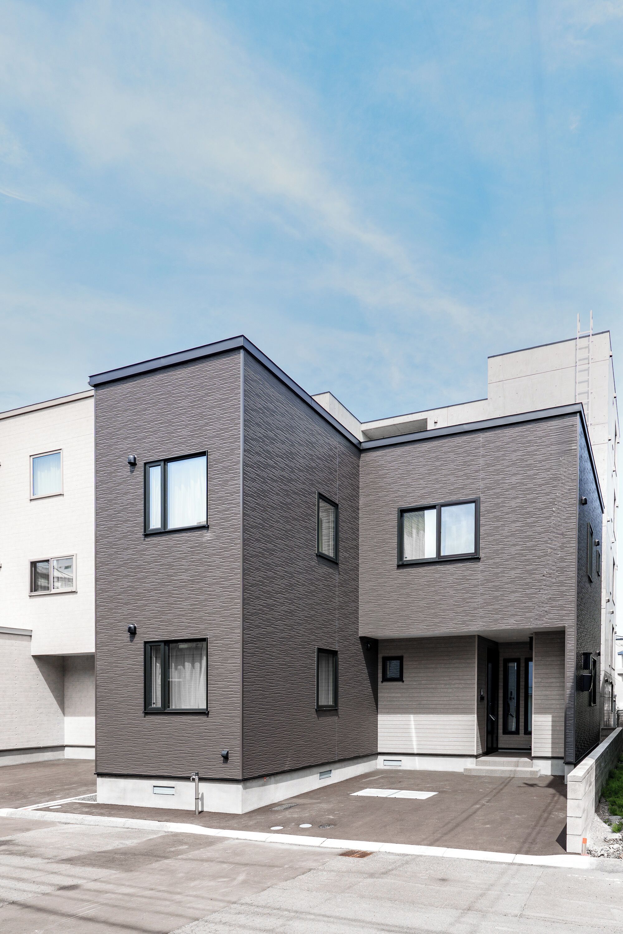 Un immeuble résidentiel moderne à deux étages, doté d’un toit plat, de grandes fenêtres et d’un design épuré et minimaliste.