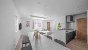 Une cuisine moderne dotée d’un îlot central, un coin repas avec une longue table et un espace de vie comprenant un canapé et une fenêtre.