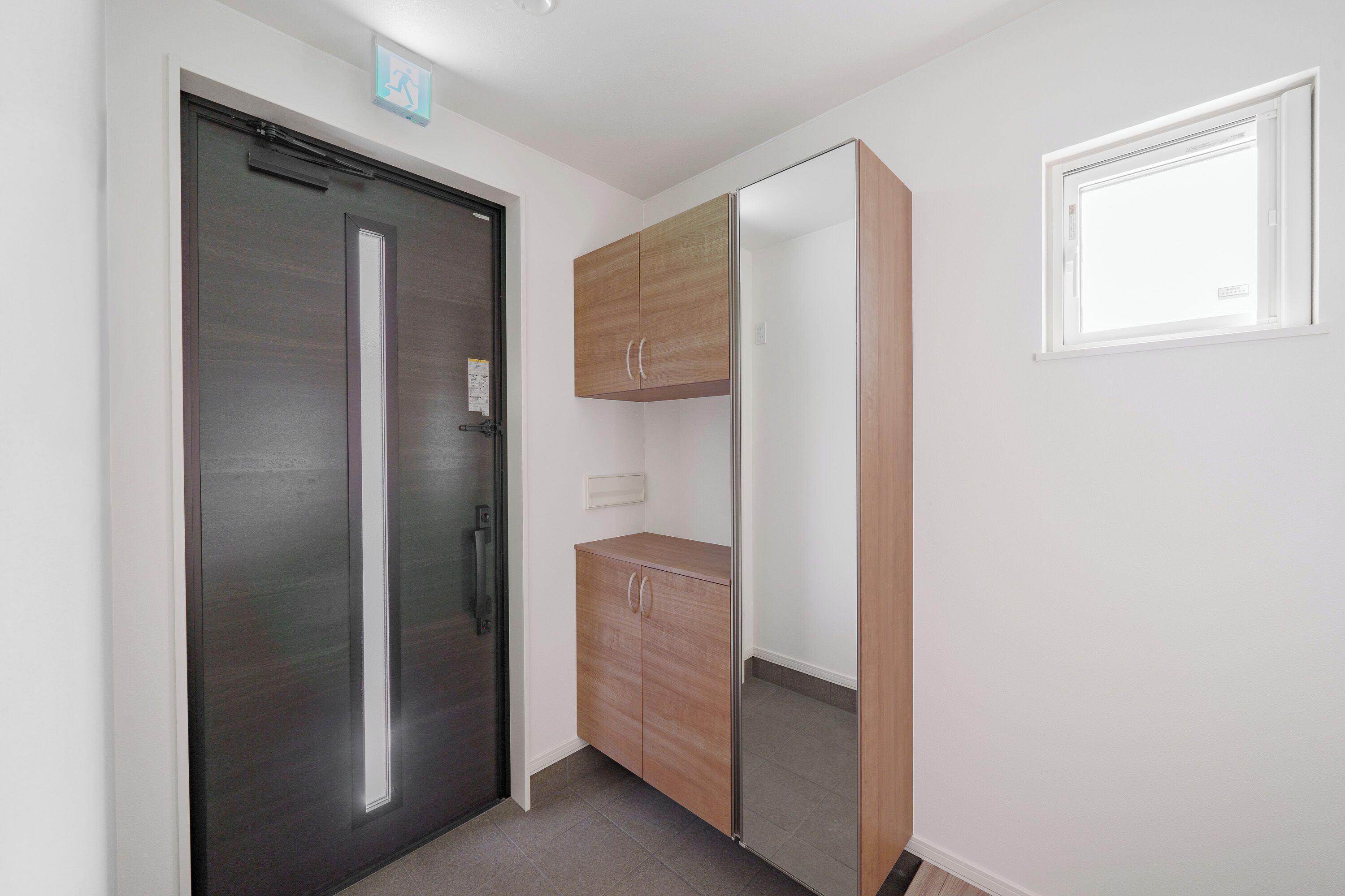 A hallway with a dark door, a wooden cabinet, and a window with blinds.