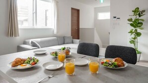 Aamiainen on katettu moderniin huoneeseen, jossa on sohva ja ruukkukasvi. Tarjolla on croissantteja, munia ja mehua.