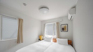 Une chambre d’hôtel comprenant un lit, une table de chevet avec une lampe, une fenêtre avec des rideaux et un appareil de climatisation.