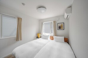 Habitación de hotel con cama, mesita de noche con lámpara, ventana con cortinas y equipo de aire acondicionado.