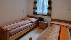 Ein Zimmer mit drei aneinandergereihten Holzbett und einem Fenster mit Vorhängen sowie einer Deckenleuchte.