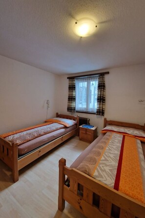 Ein Zimmer mit drei aneinandergereihten Holzbett und einem Fenster mit Vorhängen sowie einer Deckenleuchte.