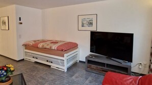 Ein Wohnzimmer mit Bett, einem roten Sofa, einem Fernseher und einem kleinen Tisch mit Blumen.