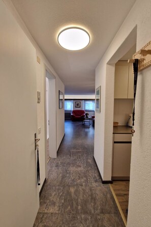 A hallway leading to a living area with a red sofa, a coffee table, and a kitchen area with cabinets.