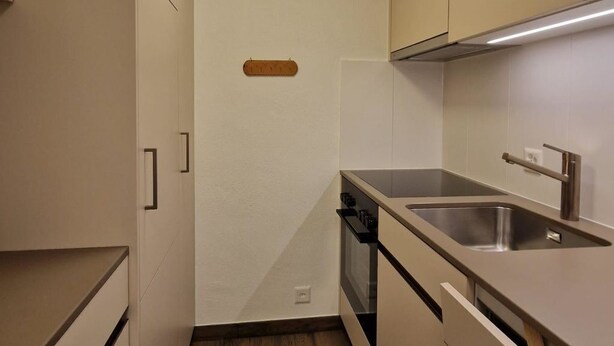 Eine kleine Küche mit eingebautem Backofen, Spüle und Schränken.