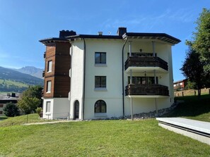 Ein mehrstöckiges Gebäude mit flachem Dach, einem Balkon im zweiten Stock und einem kleinen Eingang mit rundbogigem Durchgang.