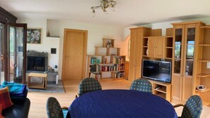 A living room with a round table, chairs, a television, and a bookshelf. - Casa Surselva Whg Marti Appartement/Fewo, Bad, WC, 2 Schlafräume by Interhome (Savognin)