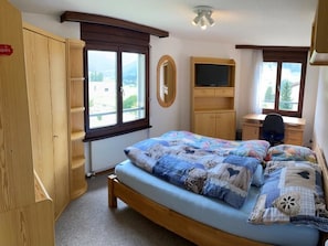A bedroom with a bed, a desk, a chair, a wardrobe, and a television.