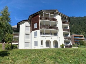 A multi-story building with balconies, a flat roof, and a hillside location.