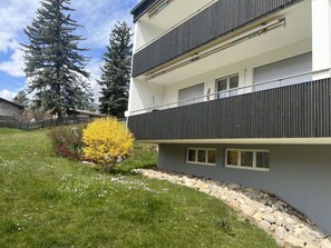 A modern multi-story building with balconies, a well-maintained lawn, and a yellow flowering shrub. - Tga Crap Alv Appartement/Fewo, Dusche, WC, 2 Schlafräume by Interhome (Savognin)