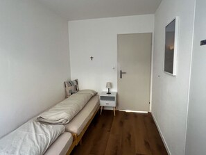 A small, single-bed room with a wooden floor, a bedside table with a lamp, and a door leading to another room. - Tga Crap Alv Appartement/Fewo, Dusche, WC, 2 Schlafräume by Interhome (Savognin)