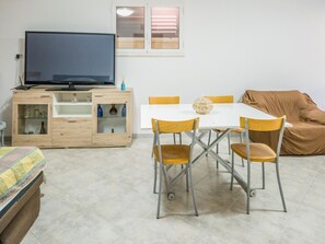 Ein Zimmer mit Fernseher auf einer Holzkommode, einem Esstisch mit Stühlen und einem Sofa.