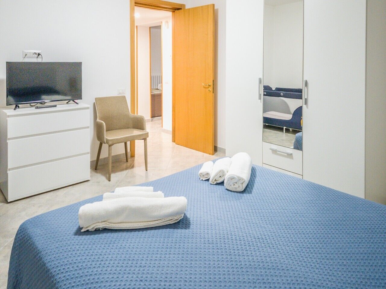 A hotel room with a bed, a TV on a dresser, a chair, and a wardrobe.