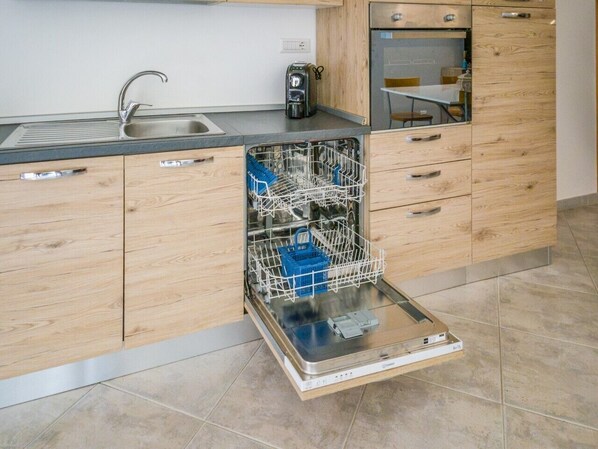 Een keuken met een vaatwasser, houten kastjes, een spoelbak en een koffiezetapparaat.