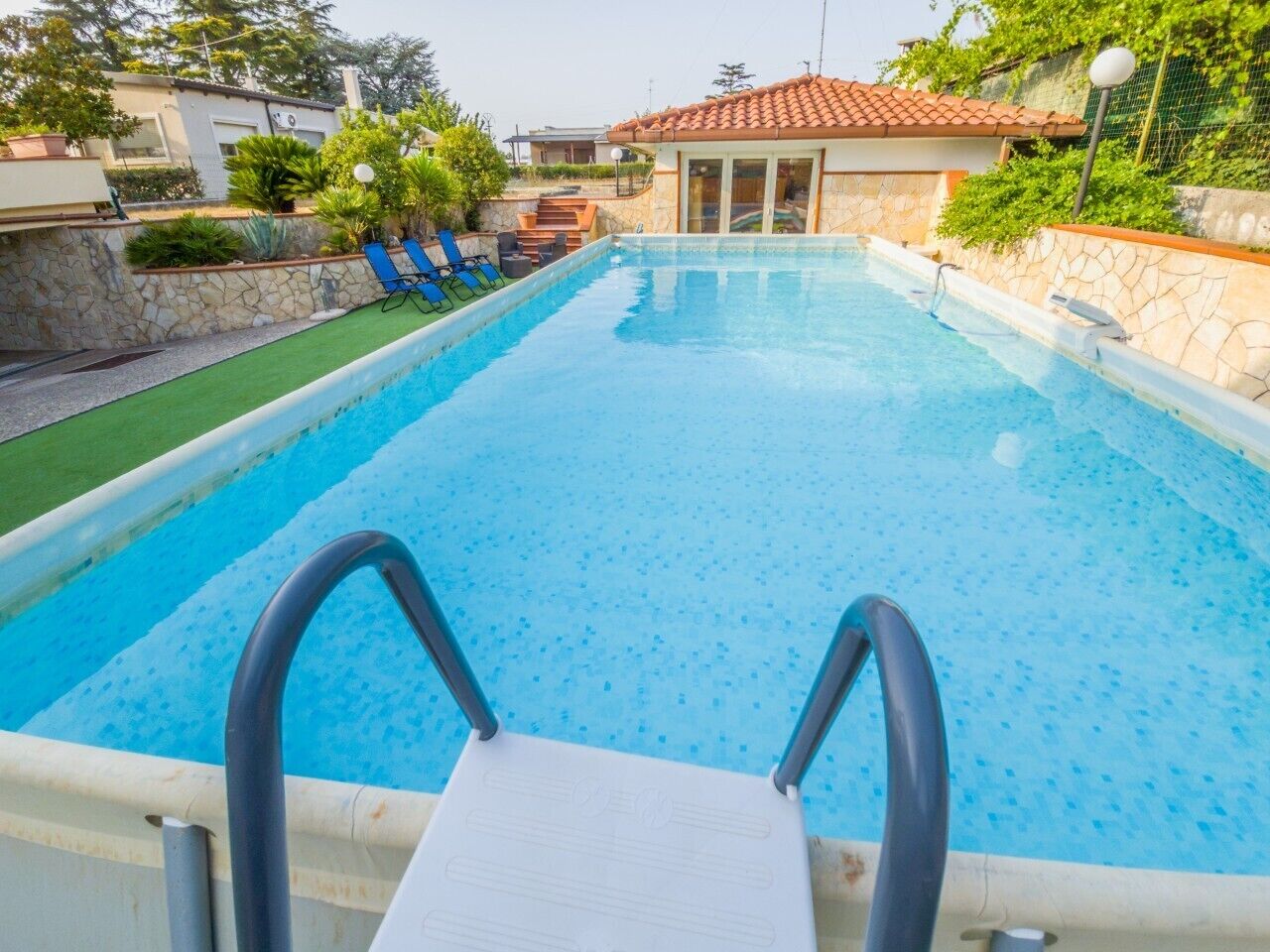 Une piscine dotée d’un plongeoir, entourée d’un mur en pierre et surmontée d’une structure à toit recouvert de tuiles.