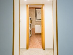 Een hal met een betegelde vloer, leidend naar een badkamer met een radiator en een kunstwerk in een lijst aan de muur.