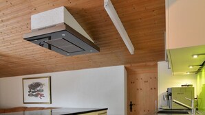 Moderni keittiö, jossa on puupalkit katossa, sisäänrakennettu uuni ja pieni keittiösaareke, jossa on pesuallas.