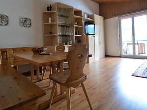 Ein geräumiges Zimmer mit einem Holzespeisetisch, Stühlen, einem Fernseher und einer Glasschiebetür zu einem Außenbereich.