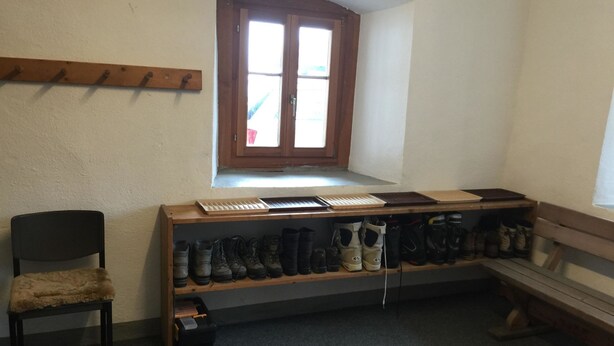 A room with a wooden bench, a chair, a shoe rack with various types of footwear, and a window with a view. - Roccabella Appartement/Fewo, Dusche oder Bad, WC, 2 Schlafräume by Interhome (Bivio)