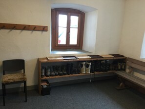 Ein Zimmer mit einer hölzernen Bank, einem Stuhl, einem Schuhregal mit unterschiedlichen Schuhen und einem Fenster mit Blick.