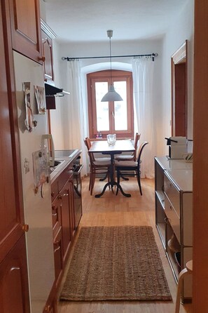 A kitchen with wooden cabinets, a dining table with chairs, a hanging light fixture, and a window with curtains. - Roccabella Appartement/Fewo, Dusche oder Bad, WC, 2 Schlafräume by Interhome (Bivio)