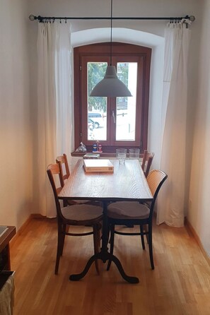 Ein Essbereich mit Holztisch, Stühlen, einer Pendelleuchte und Blick durch ein mit Vorhängen drapiertes Fenster.