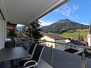 Ein Balkon mit Tisch und Stühlen mit Blick auf eine Berglandschaft und eine Kirche.