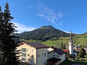 Un bâtiment doté de nombreuses fenêtres et d’un toit en pente, situé dans une vallée avec une montagne en arrière-plan.